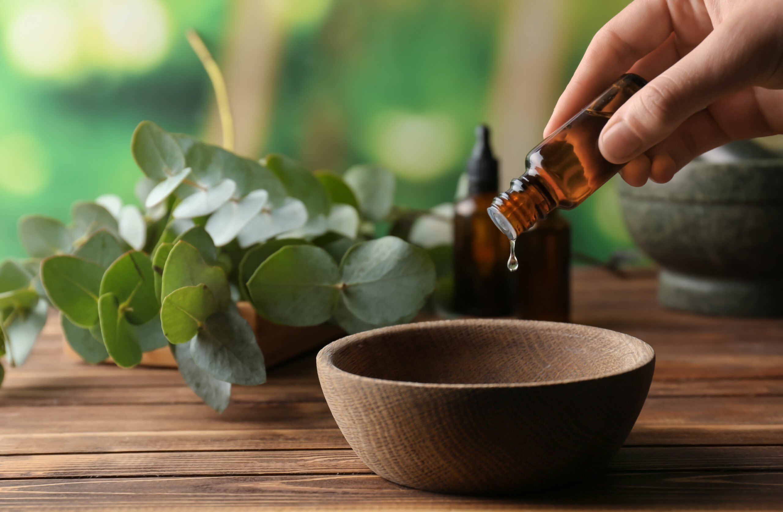 Women pouring eucalyptus essential oil into a bowl on a wooden table